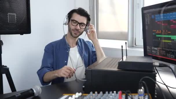 Egy fiatalember a hangstúdióban. A fickó leül az asztalhoz és beállítja a keverőpultot. Hallgasd a zenét fejhallgatón keresztül. Nyilvántartási folyamat. - Felvétel, videó
