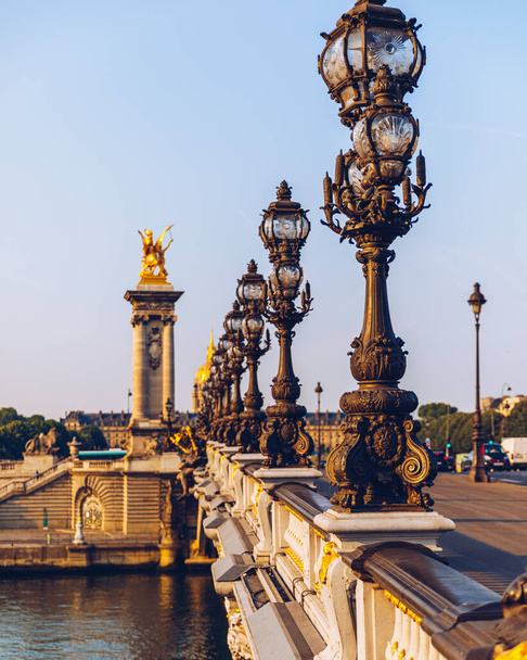 Γέφυρα Pont Alexandre III πάνω από τον ποταμό Σηκουάνα το ηλιόλουστο πρωινό του καλοκαιριού. Γέφυρα διακοσμημένη με περίτεχνα φωτιστικά Art Nouveau και γλυπτά. Η Γέφυρα του Αλεξάνδρου ΙΙΙ κατά μήκος του ποταμού Σηκουάνα στο Παρίσι, Γαλλία. - Φωτογραφία, εικόνα
