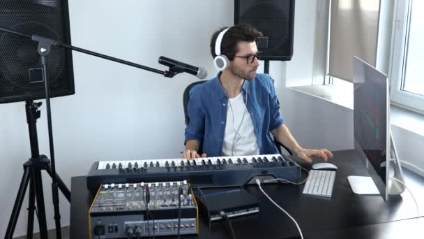 Young man in sound recording studio. Slow motion of cheerful soundman adjusting music console. Student learning how to play on keyboards. - Footage, Video