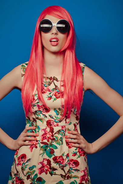 модель с розовыми волосами и большими солнечными очками на синем фоне
 - Фото, изображение