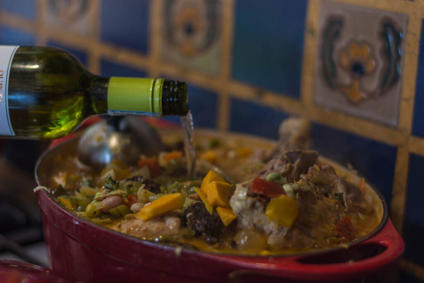 derramando vinho branco na panela em que um prato típico colombiano é cozido
 - Foto, Imagem
