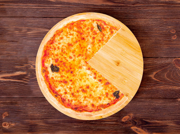 Leckere Pizza mit Mozzarella, Bocconcini und Basilikumblättern oder Pizza Margherita, ohne ein Viertel auf einer runden Holzplatte, die auf einem rustikalen Holztisch steht, von oben - Foto, Bild