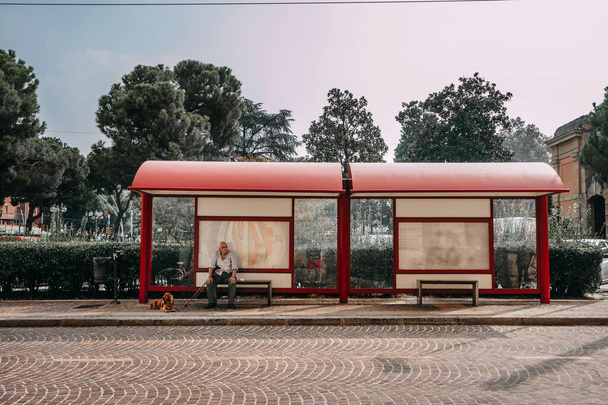 A large red bus stop complex in Bolonia with a grandfather and his dog waiting for the bus a Sunny day and trees in the background | BOLOGNA, ITALY - 17 SEPTEMBER 2018. - Zdjęcie, obraz