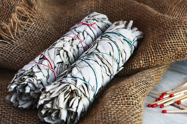 Una imagen de cerca de dos palos de salvia blanca mancha en tela de arpillera beige
.   - Foto, Imagen