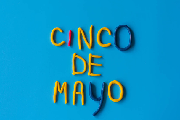 Слова CINCO DE MAYO, что означает 5 мая, сделаны из глины на синем фоне, плоская кладка. США, Мексика праздник, фон с текстом
. - Фото, изображение