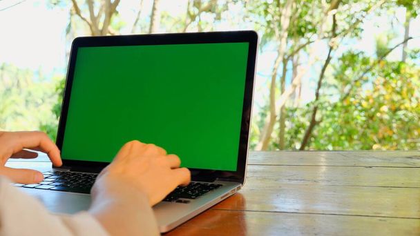 ラップトップコンピュータのキーボードに入力する女性の手の肩のショットの上に。自宅、フリーランスのコンセプト、仕事プロジェクト、執筆、ウェブコミュニケーション、デジタルノマド、緑の画面での仕事 - 写真・画像