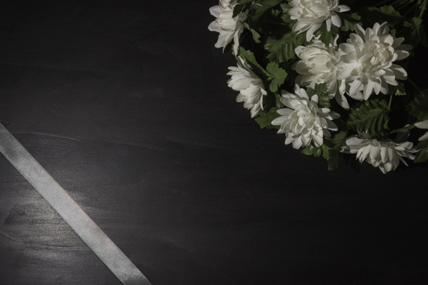 Símbolo funerario. Un ramo de flores blancas en el lado, fondo negro, espacio libre para el texto. Cinta de satén en la esquina
. - Foto, Imagen