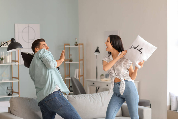 Happy young couple fighting on pillows at home - 写真・画像