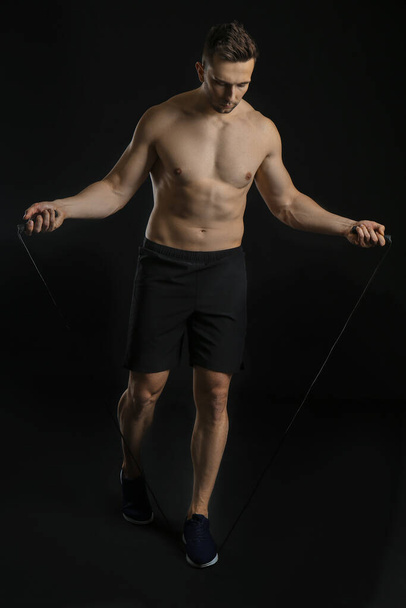 Sporty man with jumping rope on dark background - Фото, зображення