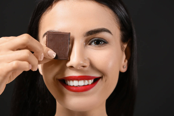 Beautiful young woman with chocolate on dark background - Foto, afbeelding