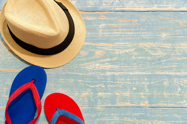 Hasır şapkalı düz plaj aksesuarları ve mavi ahşap arka planda mavi-kırmızı parmak arası terlikler. Yaz tatili konsepti. - Fotoğraf, Görsel