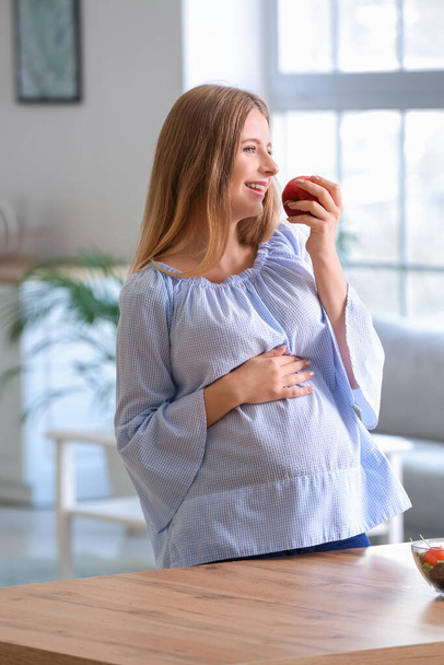 Mooie jonge zwangere vrouw met appel thuis - Foto, afbeelding
