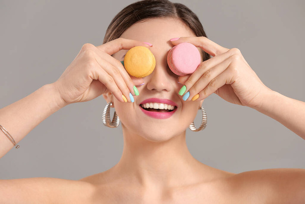 Young woman with beautiful manicure and macarons on grey background - Photo, Image