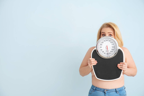 Troubled overweight woman with scales on color background. Weight loss concept - Photo, Image