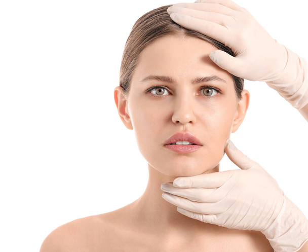 Cirujano plástico examinando la cara de mujer joven sobre fondo blanco
 - Foto, Imagen