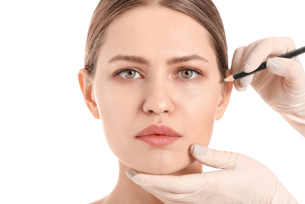 Cirurgião plástico aplicando marcas no rosto da mulher contra fundo branco - Foto, Imagem
