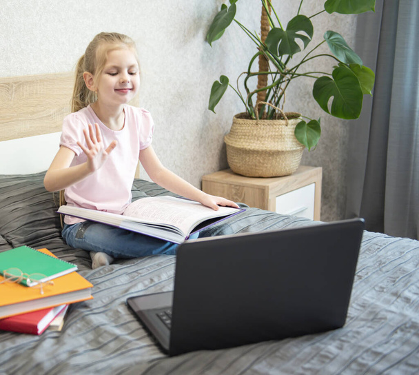 Kaukázusi lány gyermek ül az ágyban, és tanul online laptopon. Otthoni iskola, online oktatás, otthoni oktatás, karantén, koronavírus koncepció. - Fotó, kép