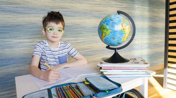 Carino studente nerd in tondo occhiali divertenti è seduto a una scrivania a una lezione di geografia. Lo studente torna a scuola dopo una lunga vacanza estiva
. - Foto, immagini