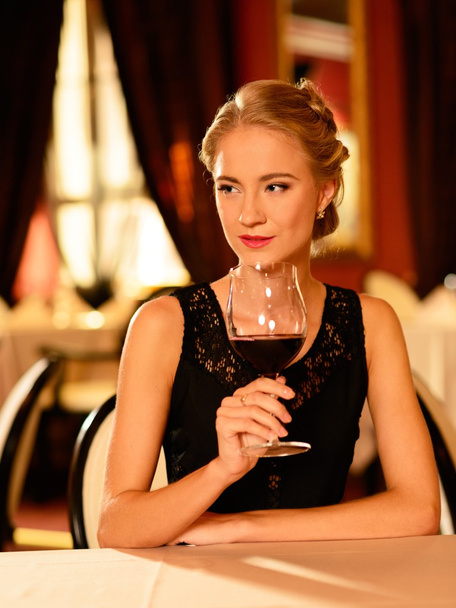 Beautiful young girl with glass of red wine alone in a restaurant - Photo, Image