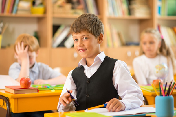Little schoolboy sitting behind school desk during lesson in school - Photo, Image