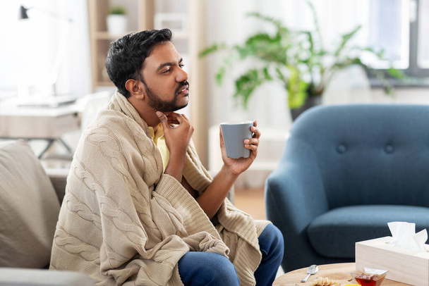 sick man with tea touching his sore throat at home - Photo, image