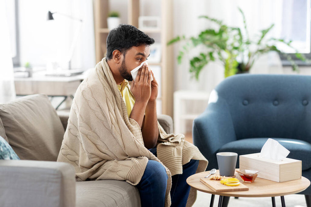 sick man blowing nose in paper tissue at home - Foto, imagen