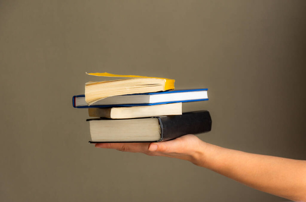 A stack of books in your hand, A day of Books, several books on one hand on a neutral background. Home leisure. Self-isolation of the house. It's good to be home. Home schooling. - Photo, Image