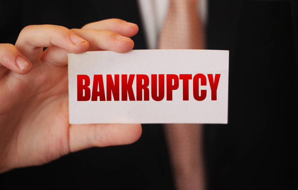 Bankruptcy on a card. Businessman holding a card with word Bankruptcy. Crisis business closing debts loss financial fiasko concept. - Photo, image