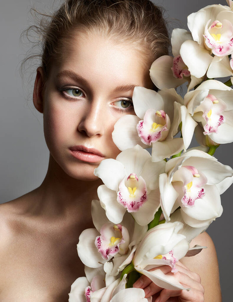 Młoda kobieta z białymi kwiatami storczyków na szarym tle - Zdjęcie, obraz