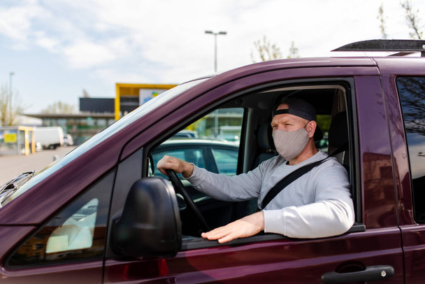 Ein Mann mit Schutzmaske am Steuer eines Autos. Ein Mann mit Schutzmaske am Steuer geht in die Apotheke. Ein Mann im grauen Pullover sitzt in einem Auto und trägt eine Maske vor einem Coronavirus. - Foto, Bild