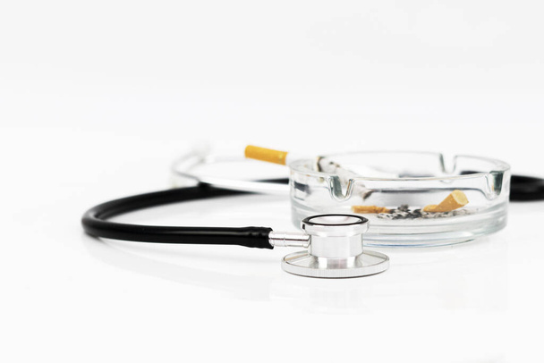 Cigarette in ashtray and stethoscope isolated in white background for medical concept and shoot in selective focusing - Photo, Image