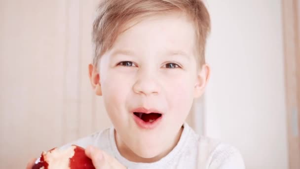 Hermosos dientes de niño sonríen y comen manzana. Lindo retrato de niño riendo. Adorable chico mirando a la cámara
. - Imágenes, Vídeo