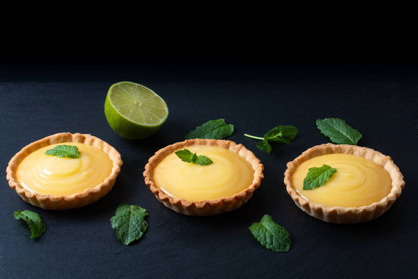 Concept alimentaire Menus bio Citron, tartes au citron vert ou mini tarte sur panneau de pierre d'ardoise noire
 - Photo, image
