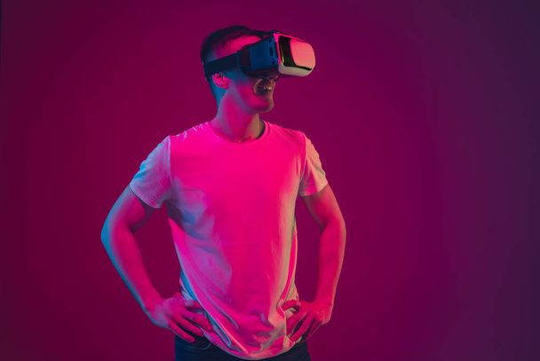 Caucasian mans portrait isolated on pink-purple studio background in neon light, playing with VR-headset - Фото, зображення