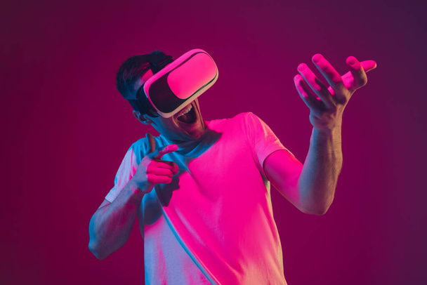 Caucasian mans portrait isolated on pink-purple studio background in neon light, playing with VR-headset - Foto, immagini