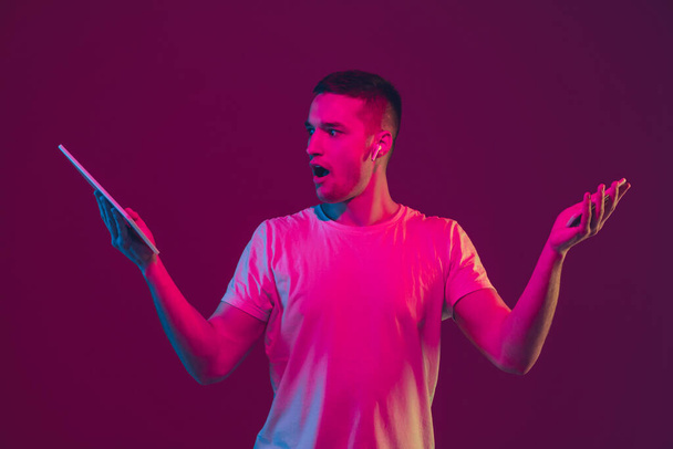 Caucasian mans portrait isolated on pink-purple studio background in neon light, using tablet - Photo, image