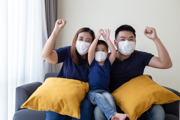 Familia asiática con máscara médica protectora para prevenir el virus Covid-19 y entregar y sentarse juntos en la sala de estar. Protección familiar contra el concepto de aire contaminado
 - Foto, imagen
