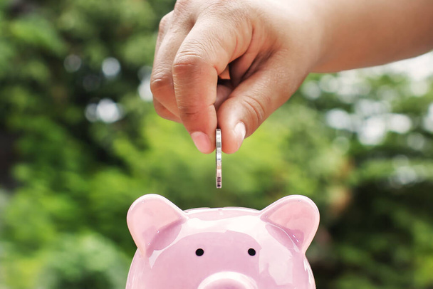 Close-up shot of a woman putting a coin in a piggy bank. Money saving concept. - Photo, Image