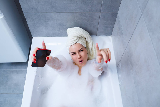 Beautiful young woman listening to music and singing while taking a bath at home. Relax after a hard day. Spa relaxing procedure. - Foto, Imagem
