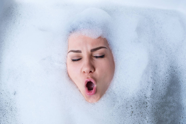 Портрет крупным планом девушки в ванной и белая пена вокруг ее лица. Разные эмоции, гримасы, женская улыбка
 - Фото, изображение