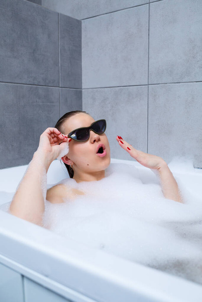 Jeune femme avec des lunettes de soleil recevant un traitement spa dans un salon de beauté, à l'intérieur d'une pièce intérieure. Détendez-vous dans la salle de bain sans linge. Soin du corps et concept de relaxation
. - Photo, image