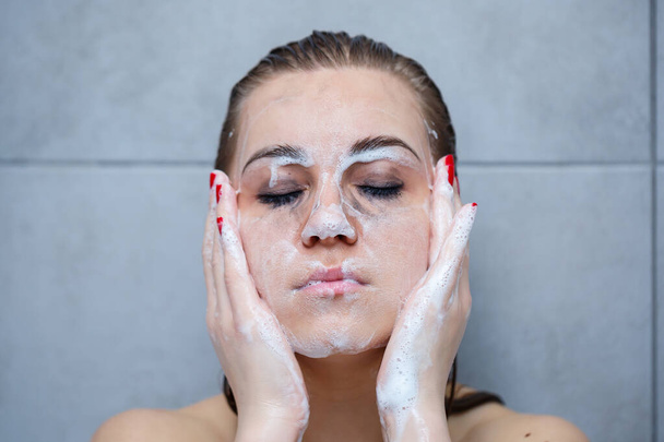 Cuidado de la piel. Mujer aplicando limpiador facial en el primer plano de la cara. Chica que usa productos cosméticos limpiadores en la piel, lavando la cara en un fondo claro
 - Foto, Imagen