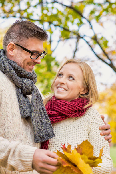 Portrait of mature couple holding maple leaves in park - Photo, Image