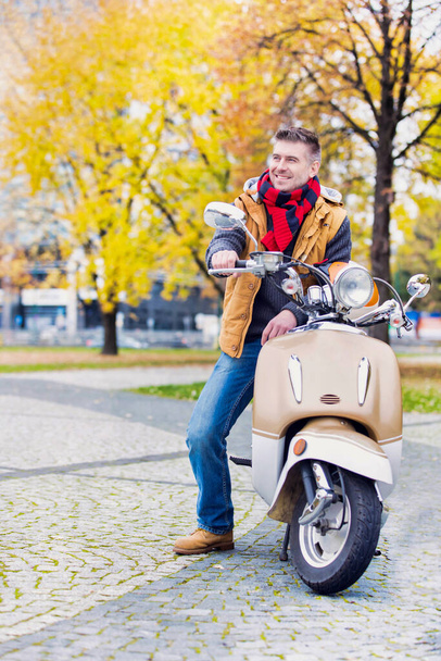 Portrait of mature attractive man sitting on motor bike while waiting in park - Fotó, kép