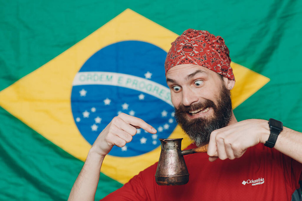Bearded man in bandana against Brazilian flag background with jezve - Photo, Image