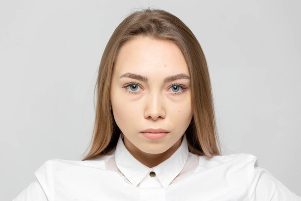 Close-up portrait of beautiful happy young attractive blonde woman in a white shirt with clean skin looking at camera against gray-white background - Фото, изображение