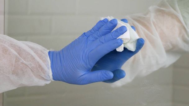 Лицо, носящее защитную одежду, дезинфицирующее зеркало в ванной комнате, очищающее салон туалетной комнаты в карантинной больнице
 - Фото, изображение