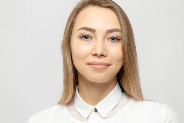 Close-up portrait of beautiful happy young attractive blonde woman in a white shirt with clean skin looking at camera against gray-white background - Foto, Imagem
