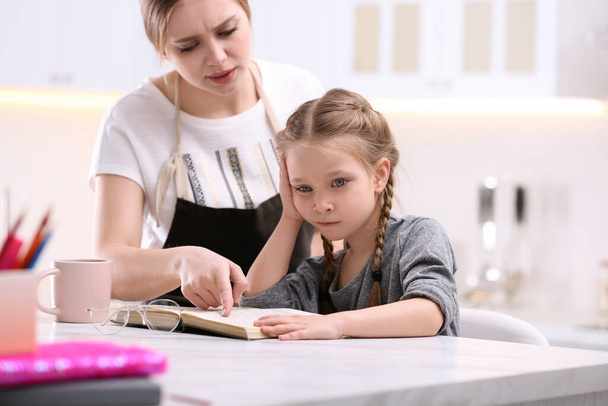 Woman helping her daughter with homework at table in kitchen - Fotoğraf, Görsel