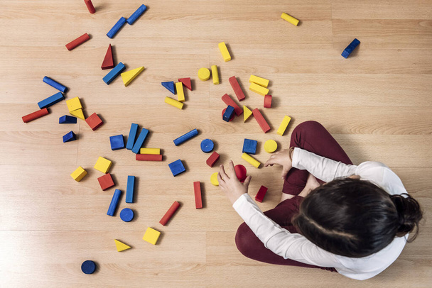 top view of an unrecognizable little girl playing at home with building blocks, concept of indoor leisure for children - Foto, afbeelding